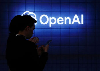 Person in front of lit-up OpenAI sign