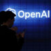 Person in front of lit-up OpenAI sign